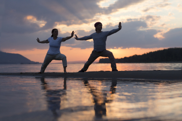 Zwei Menschen beim Qi Gong an einem See mit Sonnenuntergang im Hintergrund